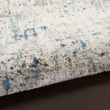 Area rug edge with textured ivory and gray pile and patches of light blue.