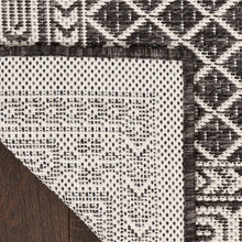 Indoor/outdoor rug corner with fringe trim and black-and-white dotted diamond pattern.