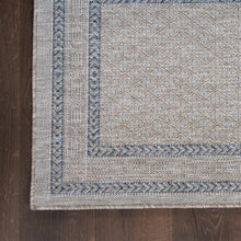 Corner detail of gray indoor/outdoor rug with blue ornamental border and flat weave