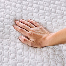 Hand smoothing a white quilted mattress topper surface with grid stitching