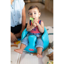 Baby holding a green silicone teether while seated in a blue activity chair