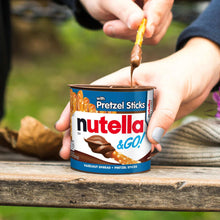 Hazelnut spread jar with pretzel sticks, brown sauce being dispensed from spoon