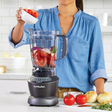 Countertop blender with clear pitcher filled with red fruit and herbs