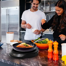 Induction cooktop on kitchen counter with pans used by people cooking