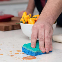 Green-and-blue scrunge sponge wiping orange marks from countertop