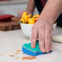 Green-and-blue scrubbing sponge wiping an orange-stained countertop