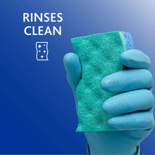 Green scrubbing sponge pad held by a blue-gloved hand over a sink