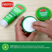 Hand applying white cream from a small tub; green cream containers and tube nearby