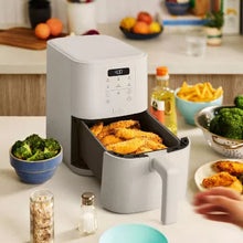 Light beige air fryer on countertop with open basket holding breaded food and hand