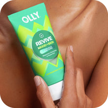 Hand using OLLY Revive body scrub on bare skin, turquoise tube held near fingers