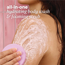 Foaming body scrub and scrubber brush lathering on shoulder, pink foam texture.