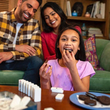 Child holding a chocolate sandwich cookie, family eating nearby