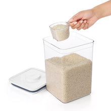 Rice measuring cup being filled from a clear container with rice