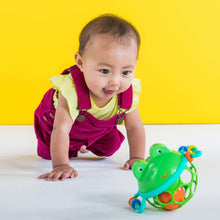 Infant crawling with green frog jingle rattle, colorful ring handles in view