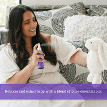 Parent holding Baby Oilogic Slumber & Sleep spray bottle on bed with white pump cap