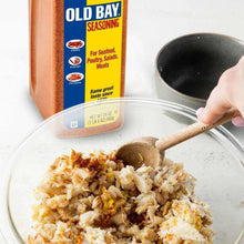 Old Bay seasoning bottle beside a bowl with spoonful seasoning-coated mixture
