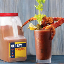 Old Bay seasoning jar beside a glass with seasoned seafood and lemon garnish