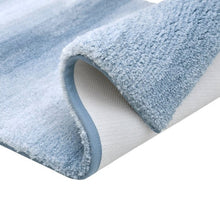 Rolled corner of blue ombre bath mat showing plush pile and backing