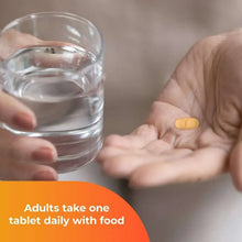 One A Day Women’s 50+ multivitamin tablet in hand with water glass