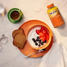 Women’s multivitamin bottle with orange cap beside plate of fruit and berries
