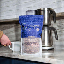 Whole bean coffee bag with blue pattern next to a white mug and coffee maker