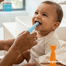 Baby using light blue silicone finger toothbrush, held on an adult finger