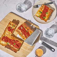 Ooni pizza spatula with dark handle beside four slice servings