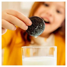Hand dipping an Oreo chocolate sandwich cookie into a glass of milk