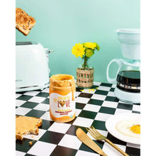Crunchy organic peanut butter jar on kitchen table with bread slice and spoon