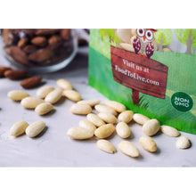 Whole blanched almonds on a light surface with green non-GMO bag in view