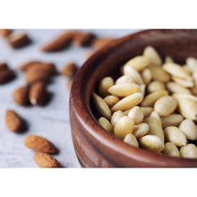 Whole blanched almonds in a wooden bowl, pale kernels filling the foreground