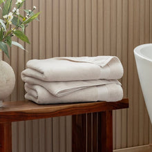 Cream organic cotton towel stack on a wooden shelf, two neatly folded towels