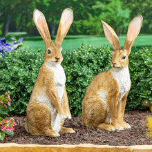 Two ornamental hare figurines, tan with white chest, sitting upright on bases