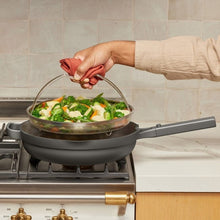 Dark gray skillet with steamer mesh basket and domed lid on a gas stove