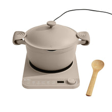 Beige Perfect Pot with lid and hot grips on an induction plate, with wooden spoon