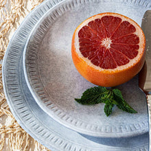 Ridged-rim blue-gray stoneware plate holding grapefruit and herbs