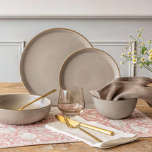 Taupe stoneware dinnerware set with bowls and plates arranged on a tablecloth