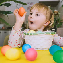 Child holding a dyed egg while using an egg decorating kit basket of colorful eggs