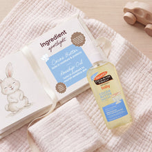 Palmer's Baby cocoa butter oil bottle with pump beside ingredient card and soft towel.