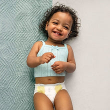 Baby standing wearing a white diaper with light blue top, Swaddlers Ultra (size 1)
