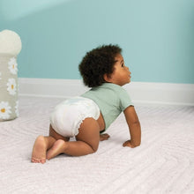 Baby on bed wearing a white diaper and green shirt, Swaddlers Ultra
