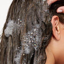Hair with foamy shampoo lather as a person massages into dark brown hair