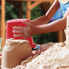 Play sand being poured from a red bucket onto hands in a sandbox