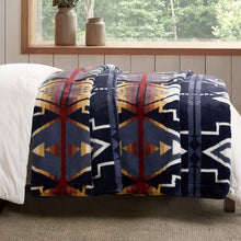 Pendleton faux fur blanket folded over a bed, showing navy, cream and rust geometric bands