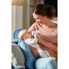 Baby bottle in use during feeding, clear bottle with teal anti-colic vent