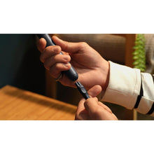 Handheld electric face shaver and trimmer in black, held between hands for use.