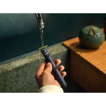Handheld electric face shaver and trimmer, black, under running water stream.