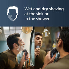 Electric shaver in use with foam-covered face at a sink mirror