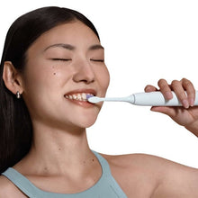 Rechargeable electric toothbrush in use, hand brushing with white handle