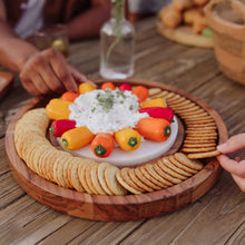 Round acacia wood serving platter with marble insert topped with vegetables and crackers